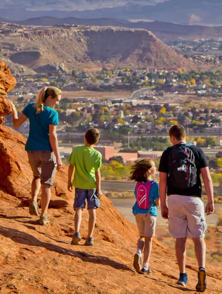 A family on a red rock formation overlooking the view of a city.