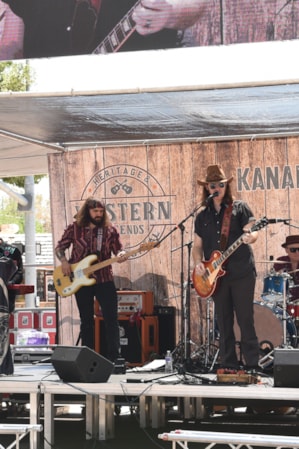 A group of band members on stage, singing, playing guitars, and playing the drums.