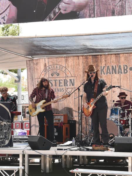 A group of band members on stage, singing, playing guitars, and playing the drums.