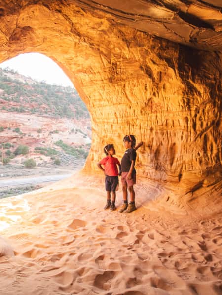 Two children standing in a sandy cave illuminated by sunlight.