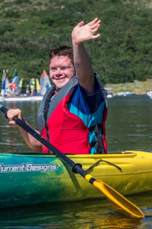 A person inside a kayak on a lake, smiling and waving.