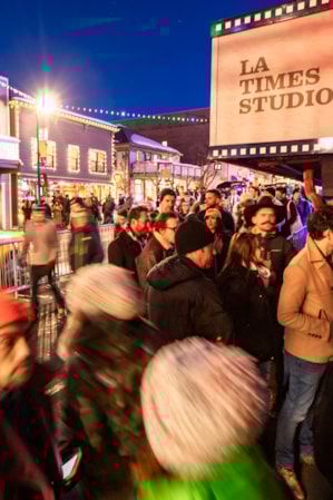 A crowd of people standing outside on the side of a street in cold weather, bundled up in winter clothing.