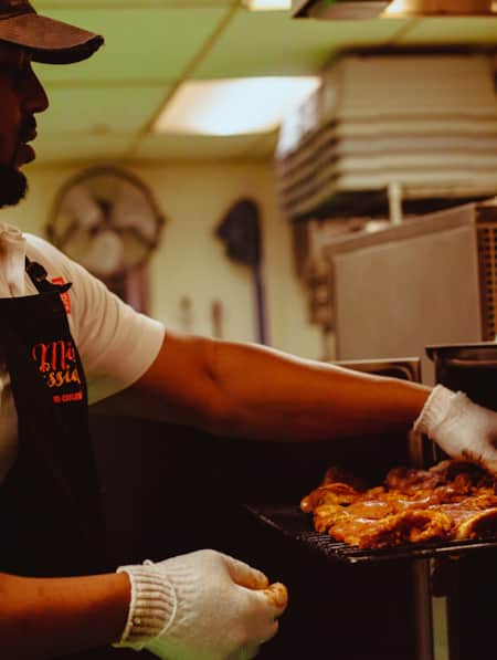 A man checking on barbecued meat in an industrial air fryer.