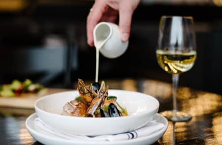 A bowl of elegantly displayed seafood, being topped with a white sauce.