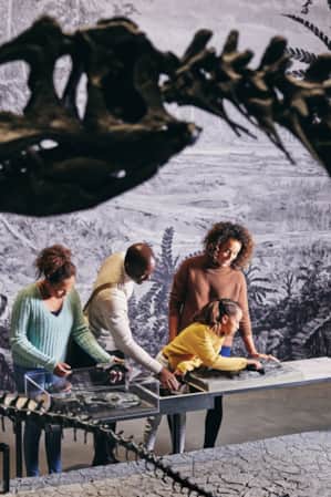 A family looking at a museum information sign with a dinosaur skeleton in front of them.