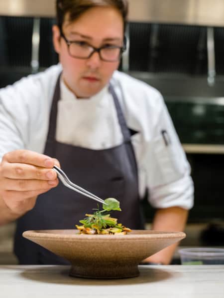 A chef adding the final garnish to a dish in a restaurant kitchen.