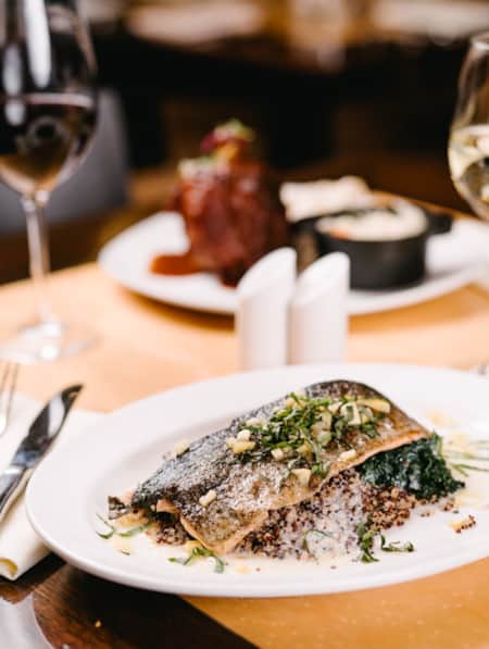 A table set with silverware, wine glasses, and a plate of pan-seared trout.