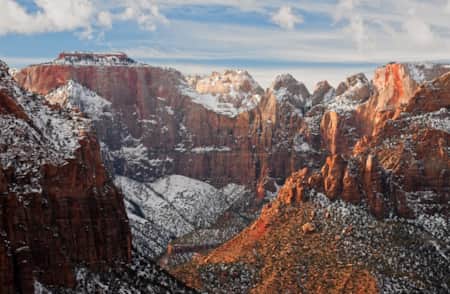 A valley surrounded by massive red rock cliff faces, lightly dusted with snow.