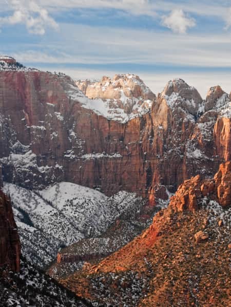 A valley surrounded by massive red rock cliff faces, lightly dusted with snow.
