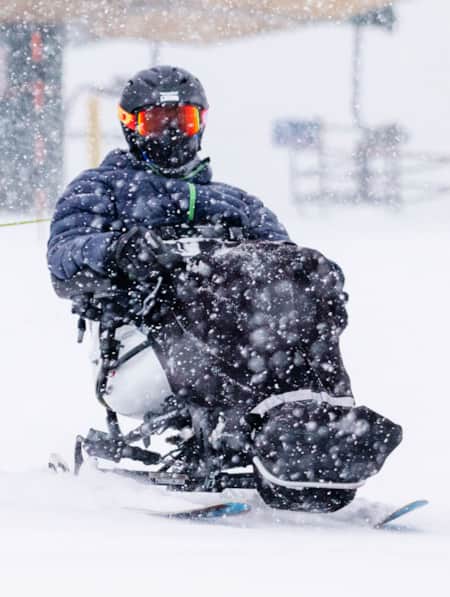 An adaptive skier skiing away from a ski lift during a snowstorm.