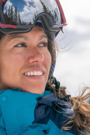 A headshot of a woman in ski clothes and a ski helmet, smiling and glancing to the side.