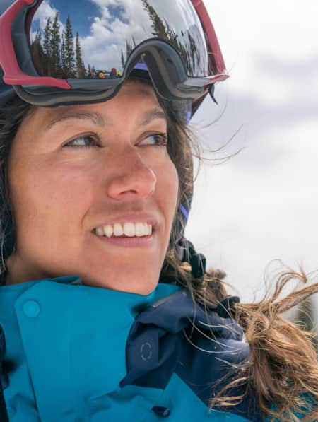 A headshot of a woman in ski clothes and a ski helmet, smiling and glancing to the side.
