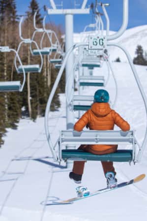 The back view of a snowboarder on a ski lift, ascending the mountain.