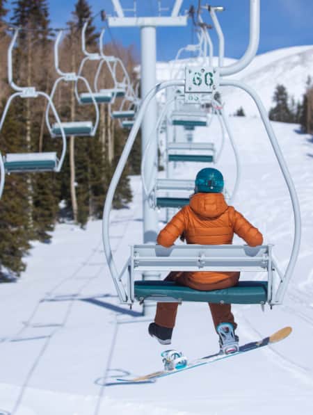 The back view of a snowboarder on a ski lift, ascending the mountain.