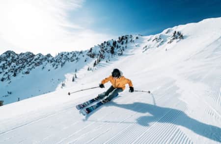 A skier making a big turn on a freshly groomed run, leaning into the turn.