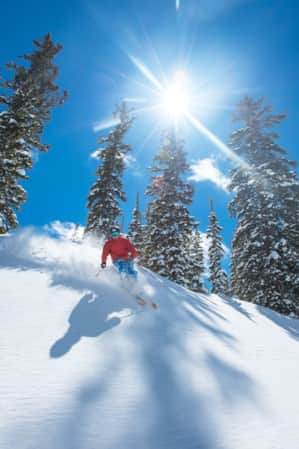 A man in a red winter jacket skiing down a mountain slope on a clear blue sky day.