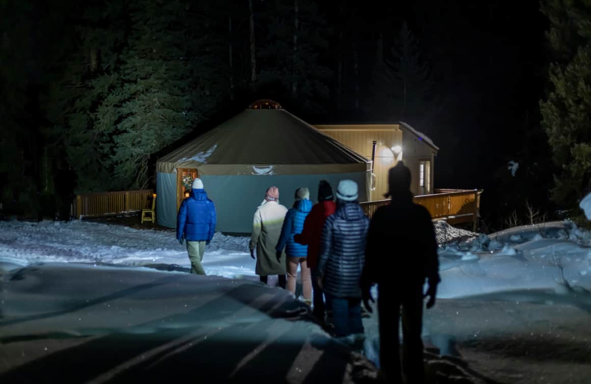 The journey to The Yurt at Solitude begins with a guided snowshoe trek through a serene, moonlit forest.
