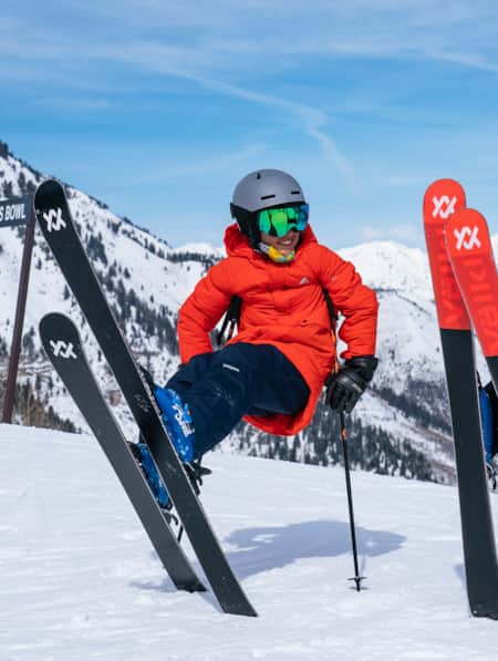 Two kids in ski gear on top of a mountain, propping themselves up with their skis and poles.