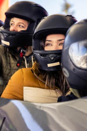 Four people wearing helmets riding a bobsled.