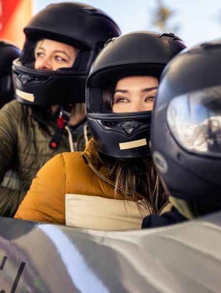 Four people wearing helmets riding a bobsled.