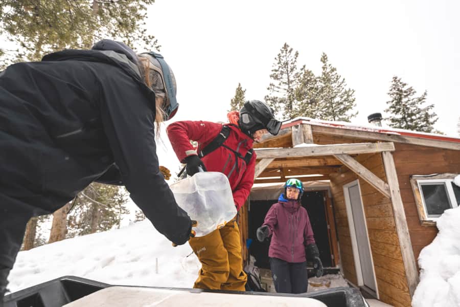 Shaun Deutschlander, Rachael Burks and Melissa Fields unload gear from the snowmobiles at the yurt.