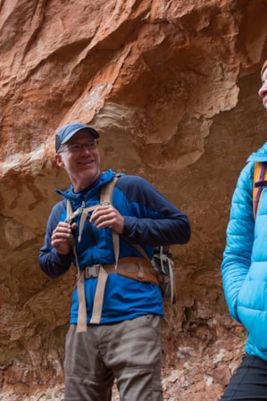 Three people in warm hiking clothing standing in front of a large red rock, talking to one another.