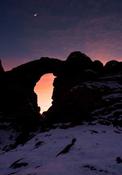 Turret Arch in Moab glows beneath a waxing crescent moon.
