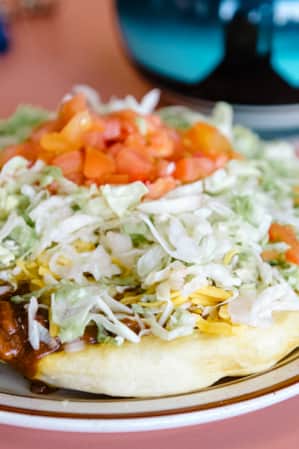 A plate of Navajo fry bread consisting of fried dough, shredded lettuce, beans, cheese, and chopped tomatoes.