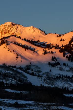 A range of snowy mountains with the setting sun casting a golden glow on the peaks.