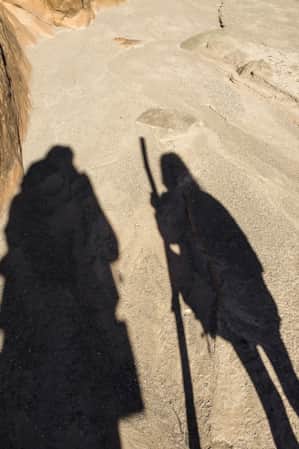 Shadows of two people hiking on a trail.