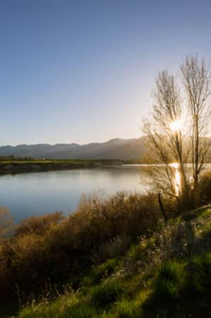 A sunrise over mountains with a lake in the foreground, surrounded by green hills.