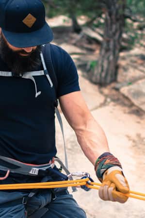 A man outside, wearing a climbing harness, is belaying himself.