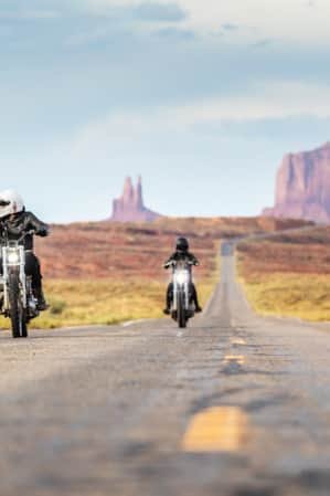 Two people riding motorcycles on a long, straight desert road."