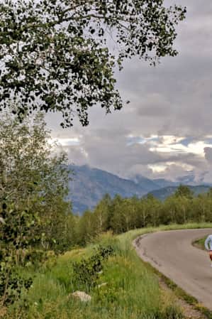 A person cycles on a road surrounded by aspen trees and mountains.