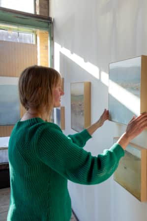 A woman hanging a piece of art in an art gallery.
