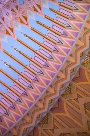 Close-up shot of a ceiling designed in an Art Deco theme, featuring intricate patterns in light pastel colors.