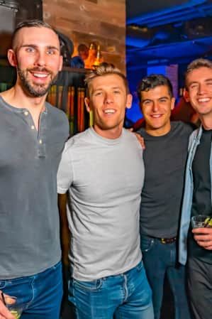 Four men standing together in a bar, smiling and looking at the camera.