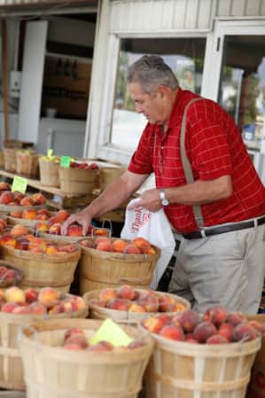A man hand-picking peaches from circular wooden baskets at a farm stand.