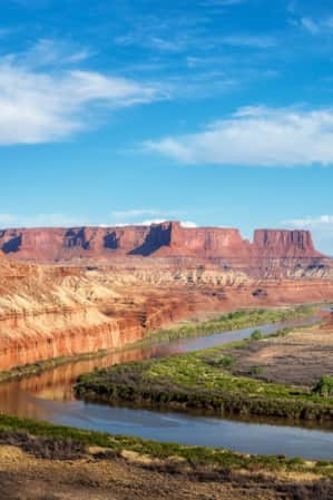An expansive view of red rock monuments with a river flowing through.