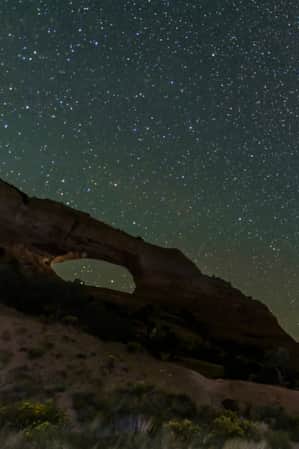 A natural bridge illuminated by the stars in the night sky.