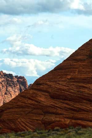 The silhouettes of two people at the top of a large red mountain during the day.