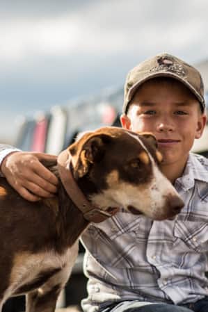 A young boy with his arm around a dog standing beside him.