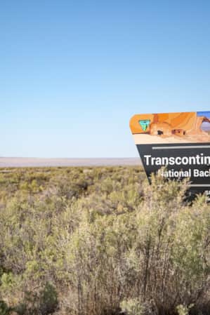 A sign in an open field of small shrubs reading "Transcontinental Railroad National Backcountry Byway."