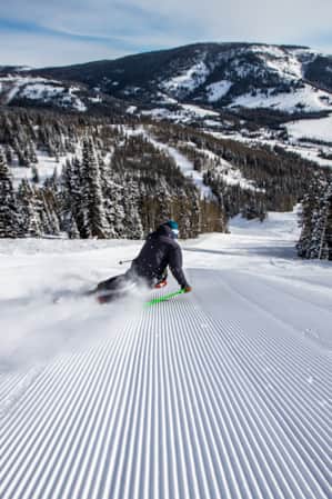 A skier making a big turn on a freshly groomed run, leaning into the turn.