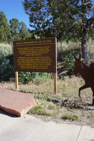 A sign explaining 'The Old Spanish National Trail' behind a paved trail, with wrought iron silhouettes of mules in the foreground.