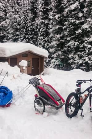 A brown yurt situated by a campsite bathroom, surrounded by snow, with a mountain bike in front of the yurt.