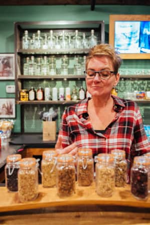 A woman standing behind a display of small glass jars filled with spices.