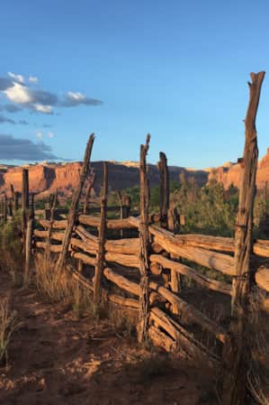 An old fence made of rustic wood in front of an expansive landscape of red rock monuments and plateaus.