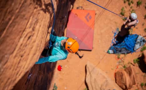 Two people help a woman boulder a canyon wall.