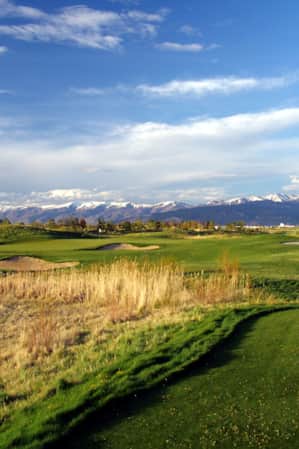 A golf course with mountains in the backdrop and houses on a hill overlooking the course.